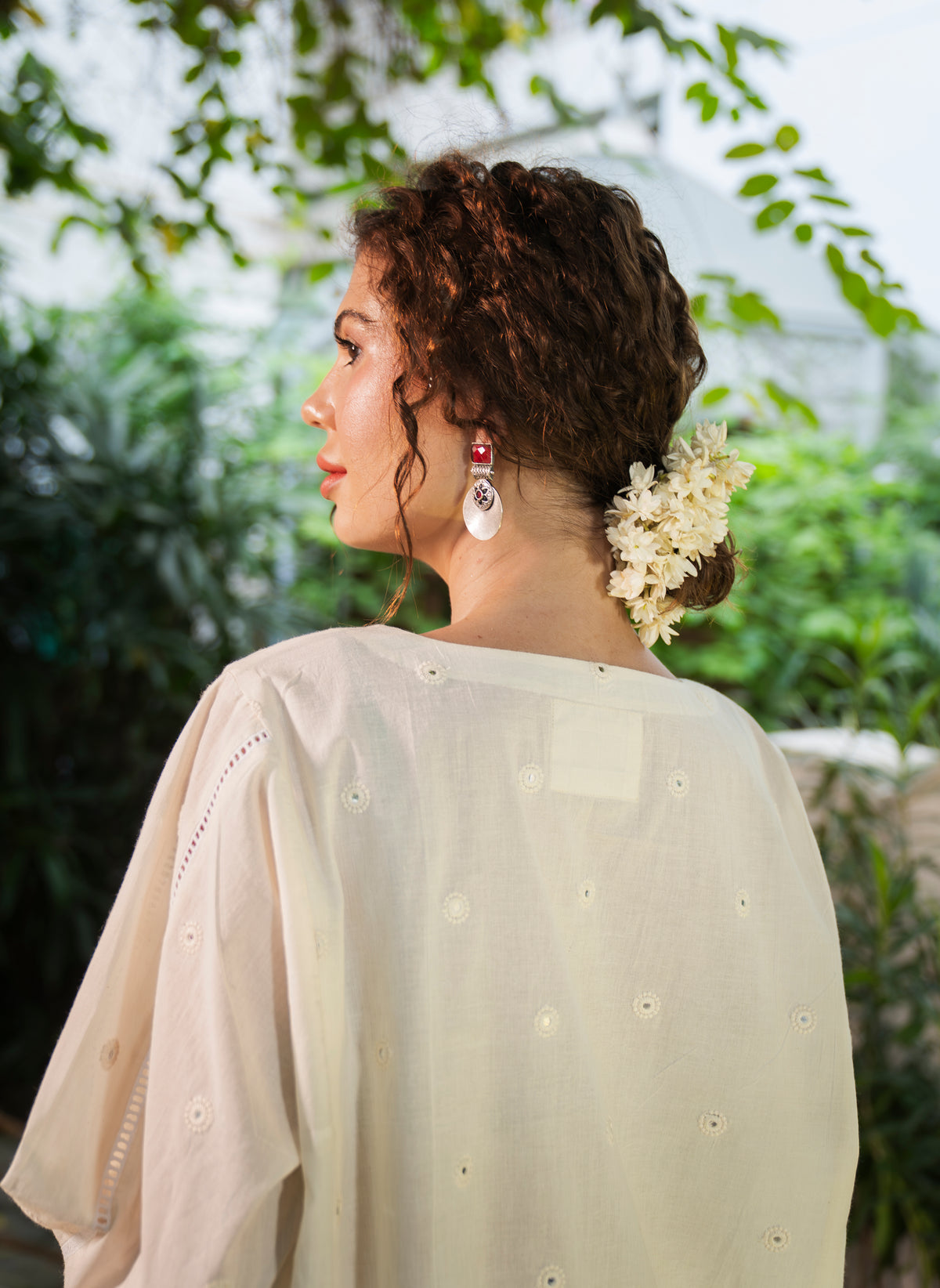 Woman wearing a light-colored outfit with floral hairpiece against a blurred natural background